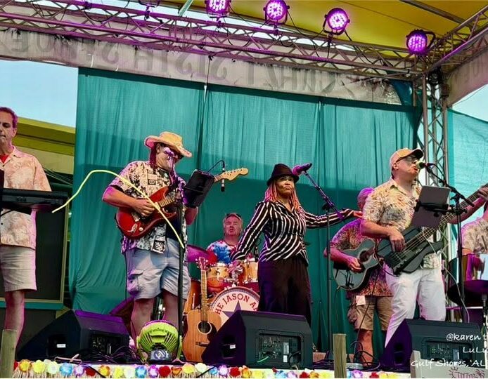 5 Live band performing onstage with a guest vocalist at an outdoor event.
