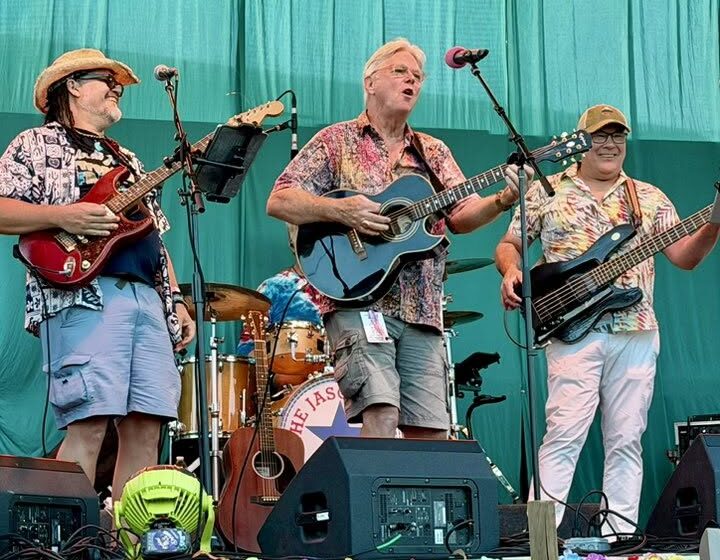 7 Three musicians performing guitar, bass, and drums together onstage.